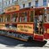A trolley car with a sign that reads Mana Riga stopped next to a neoclassical building